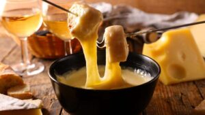 Un clásico suizo para compartir: La fondue de queso, acompañada de copas de vino blanco y una cesta con pan, es ideal para reuniones sociales.

