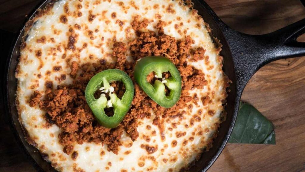 Queso fundido con chorizo servido en una sartén de hierro fundido, con una rodaja de jalapeño en el centro para un toque picante.

