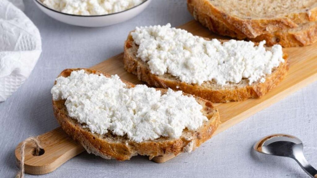 Rebanadas de pan integral con una generosa capa de queso cottage, destacando la textura cremosa y suave del queso fresco.