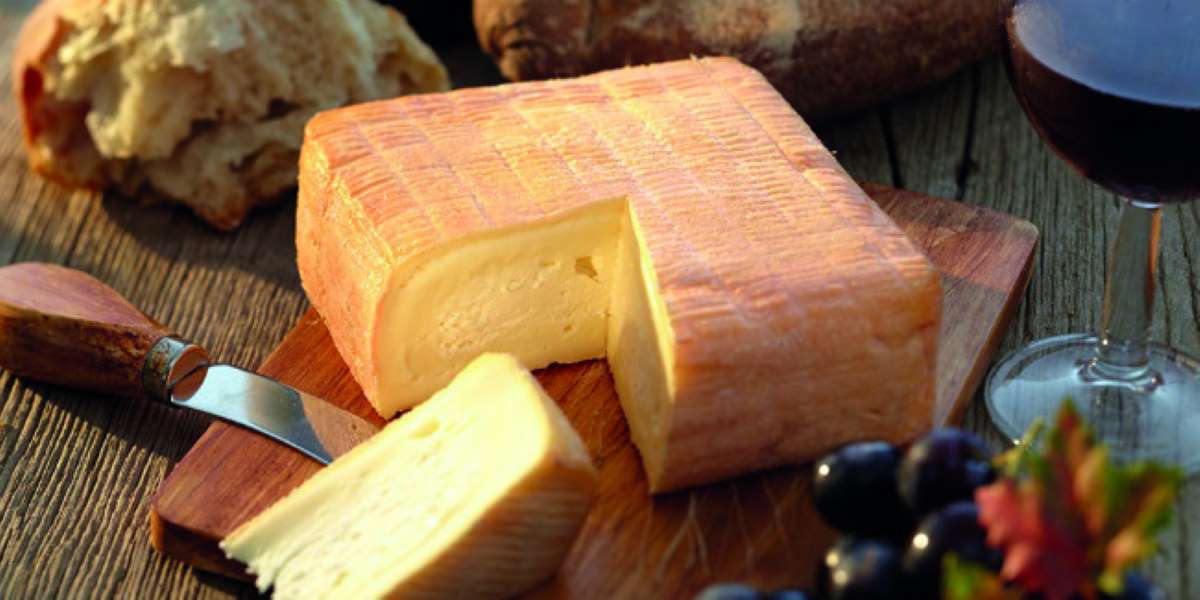 El Vieux Boulogne, conocido como el queso más oloroso del mundo, se muestra aquí con su característica corteza lavada con cerveza, acompañado de una copa de vino tinto y uvas frescas, listo para ser degustado.

