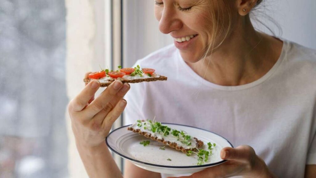 Una rebanada de pan integral con queso crema, tomate cherry y brotes verdes: una opción saludable y balanceada para el desayuno.